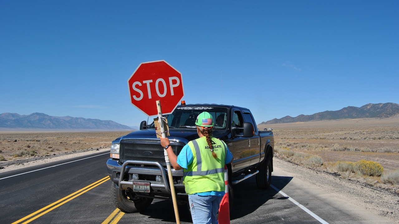 A flagger stopping a truck on a remote dessert highway.